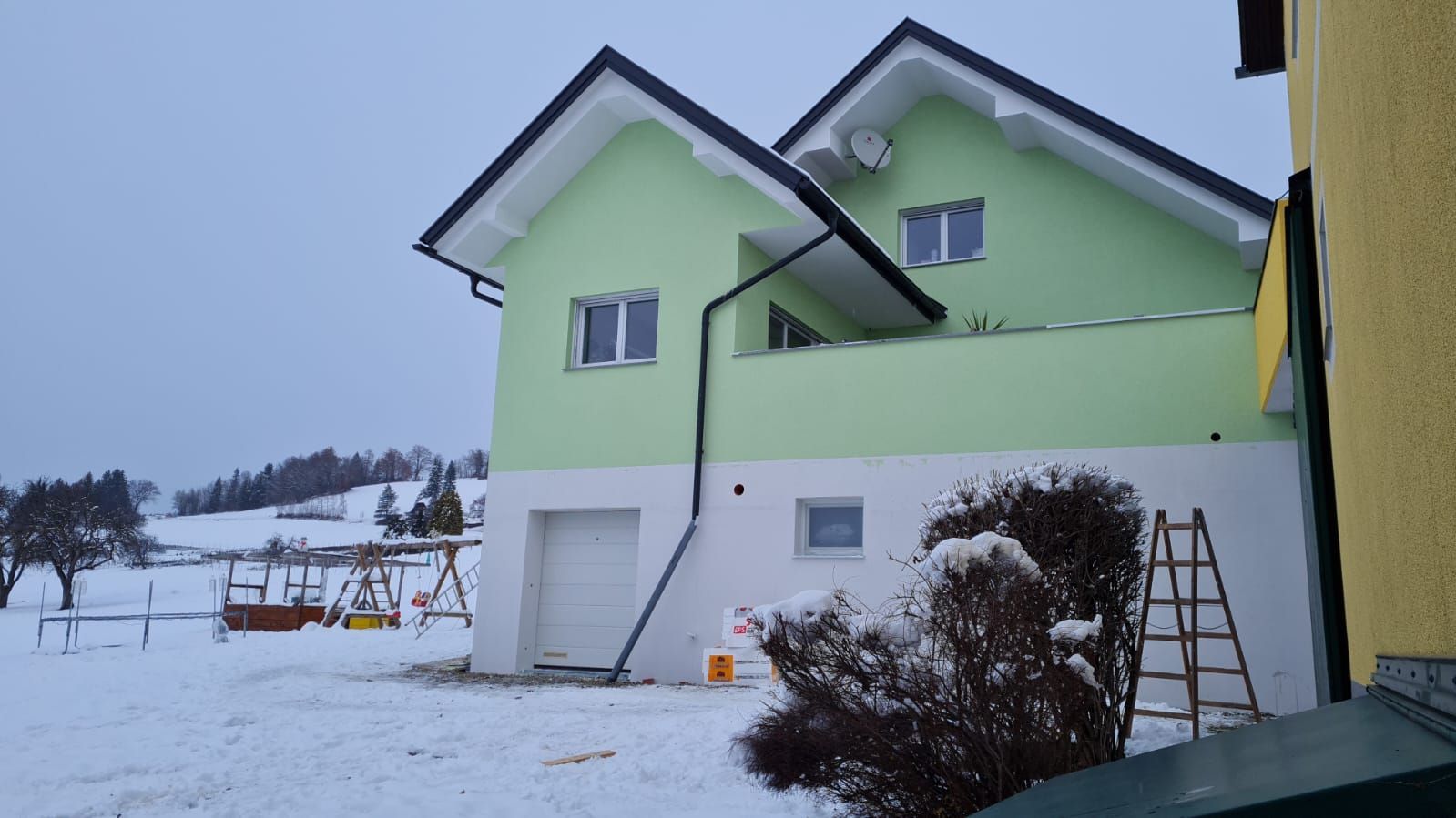 Ein grün-weißes Haus im Schnee mit einer Leiter davor