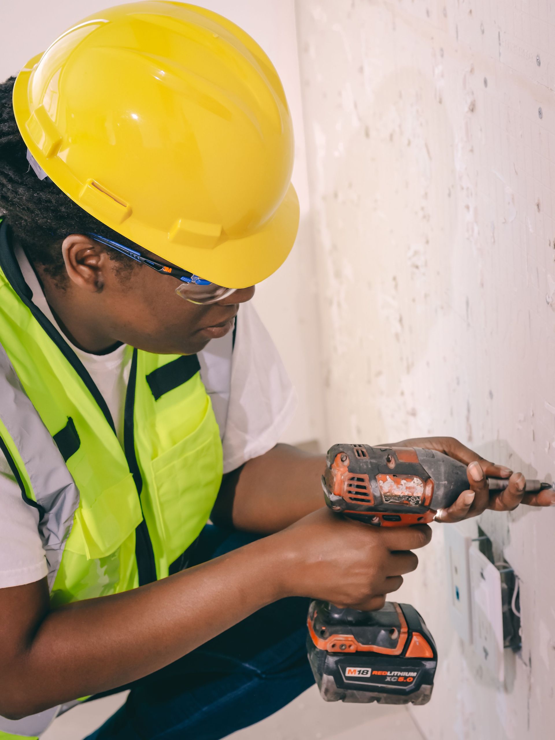 Worker in yellow hard hat using a cordless drill to install an electrical outlet in a wall