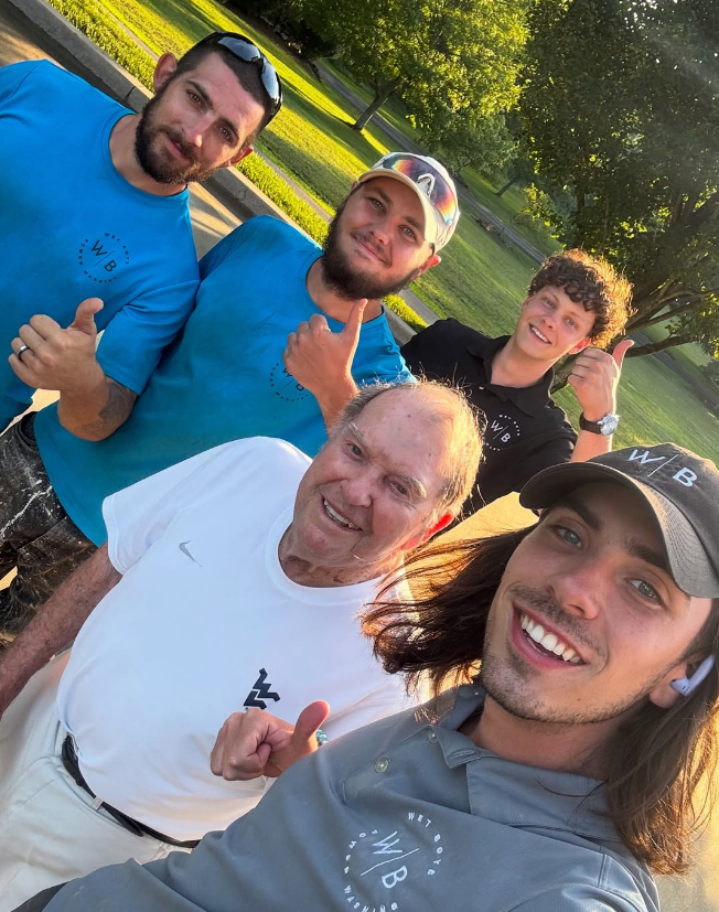 Five friends smiling and posing for a selfie in a sunny park.