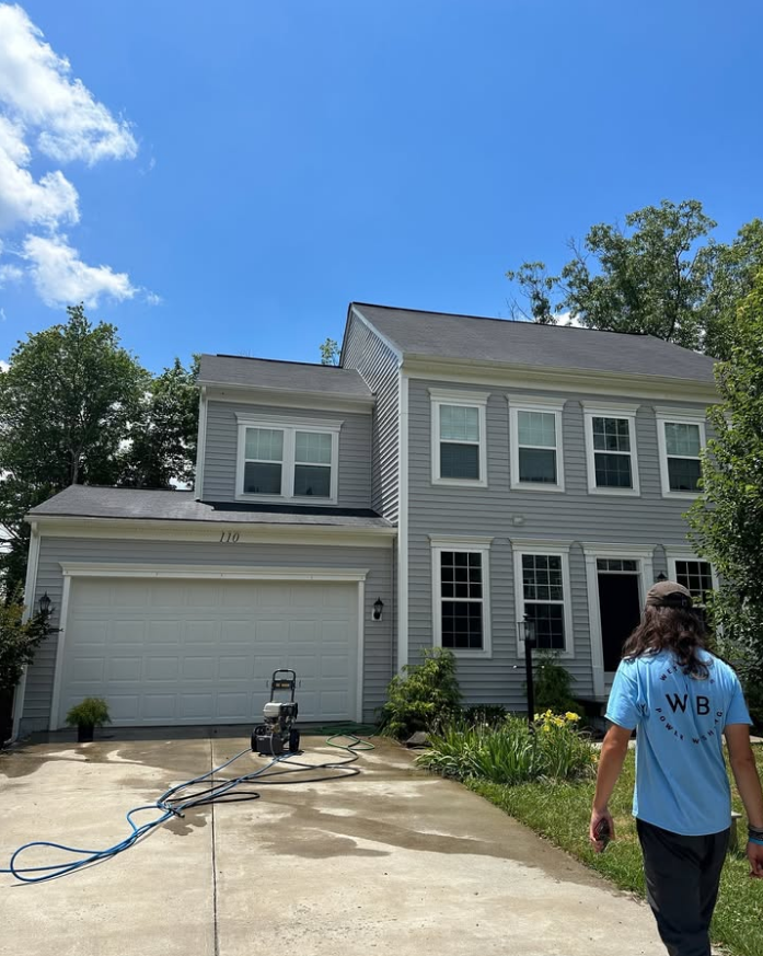 Two-story gray house with garage, driveway, and person walking in foreground under blue sky