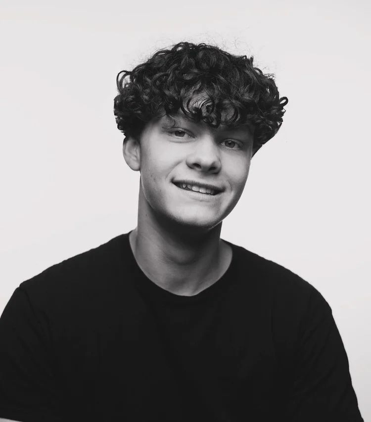 Smiling person with curly hair in a black shirt against a plain light background