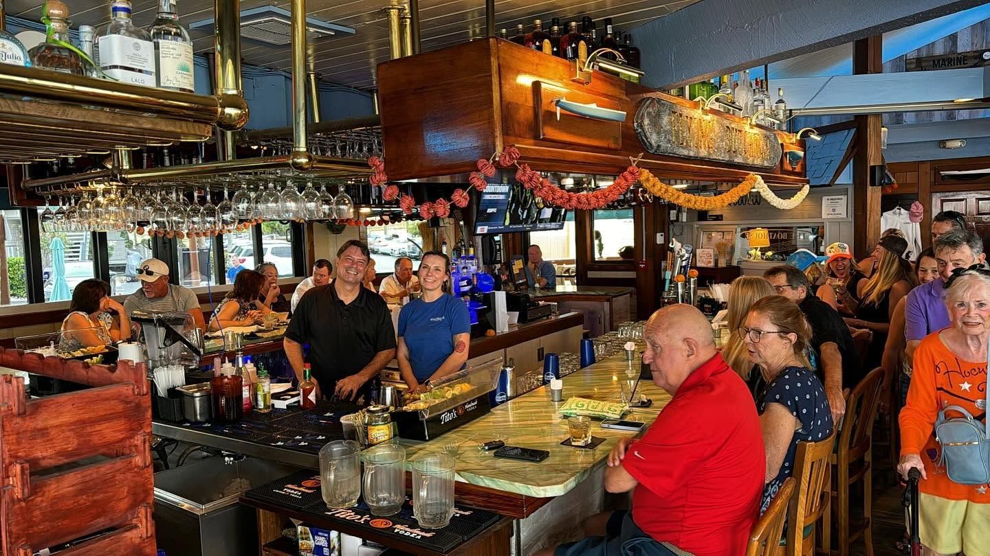 Crowded restaurant bar with diners seated at tables under hanging copper lights