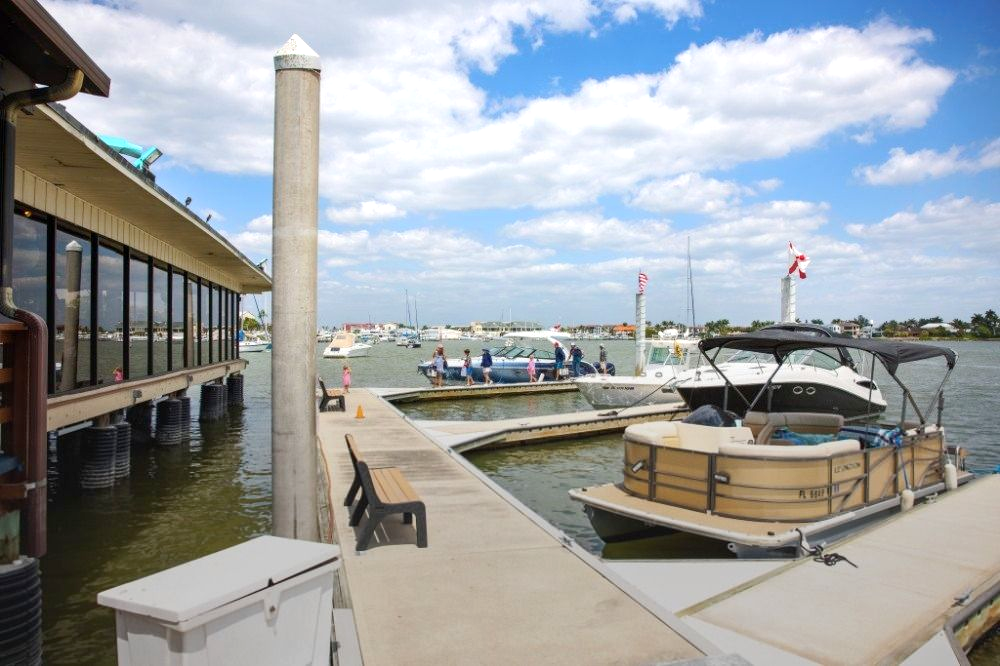 Marina dock with boats, covered pontoon, and waterfront restaurant under a cloudy blue sky