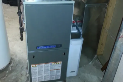 A furnace is sitting in a basement next to a water heater.
