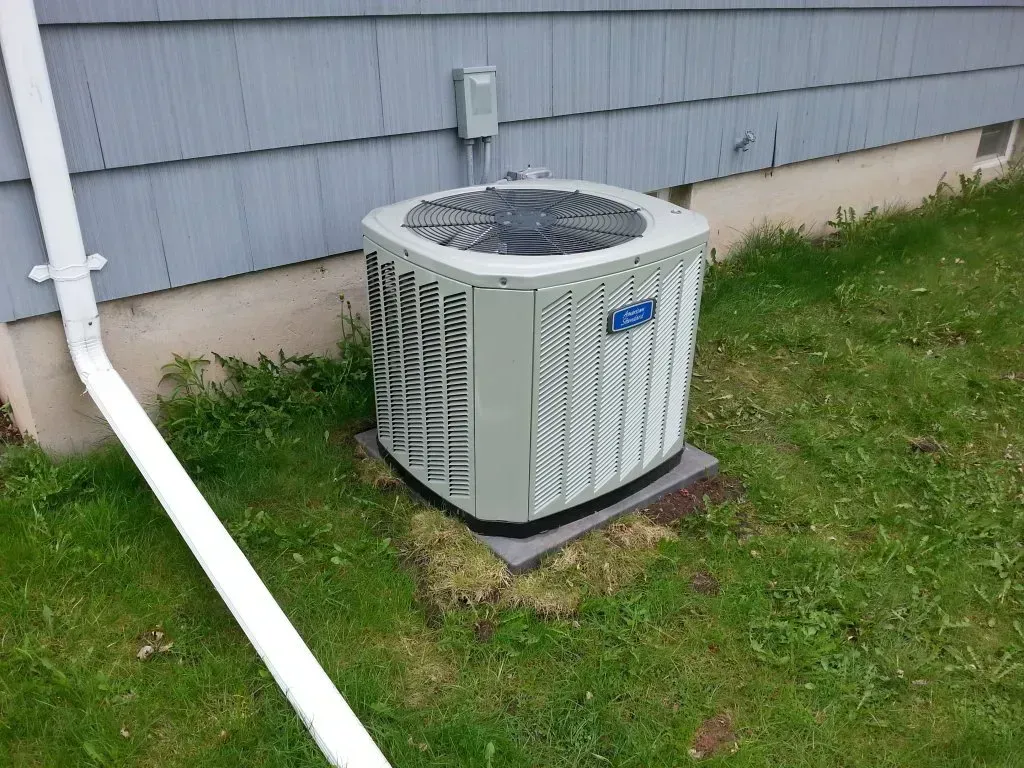 An air conditioner is sitting in the grass next to a house.