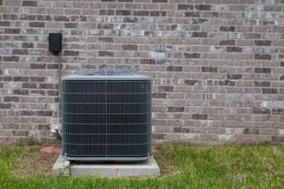 An air conditioner is sitting on the side of a brick building.
