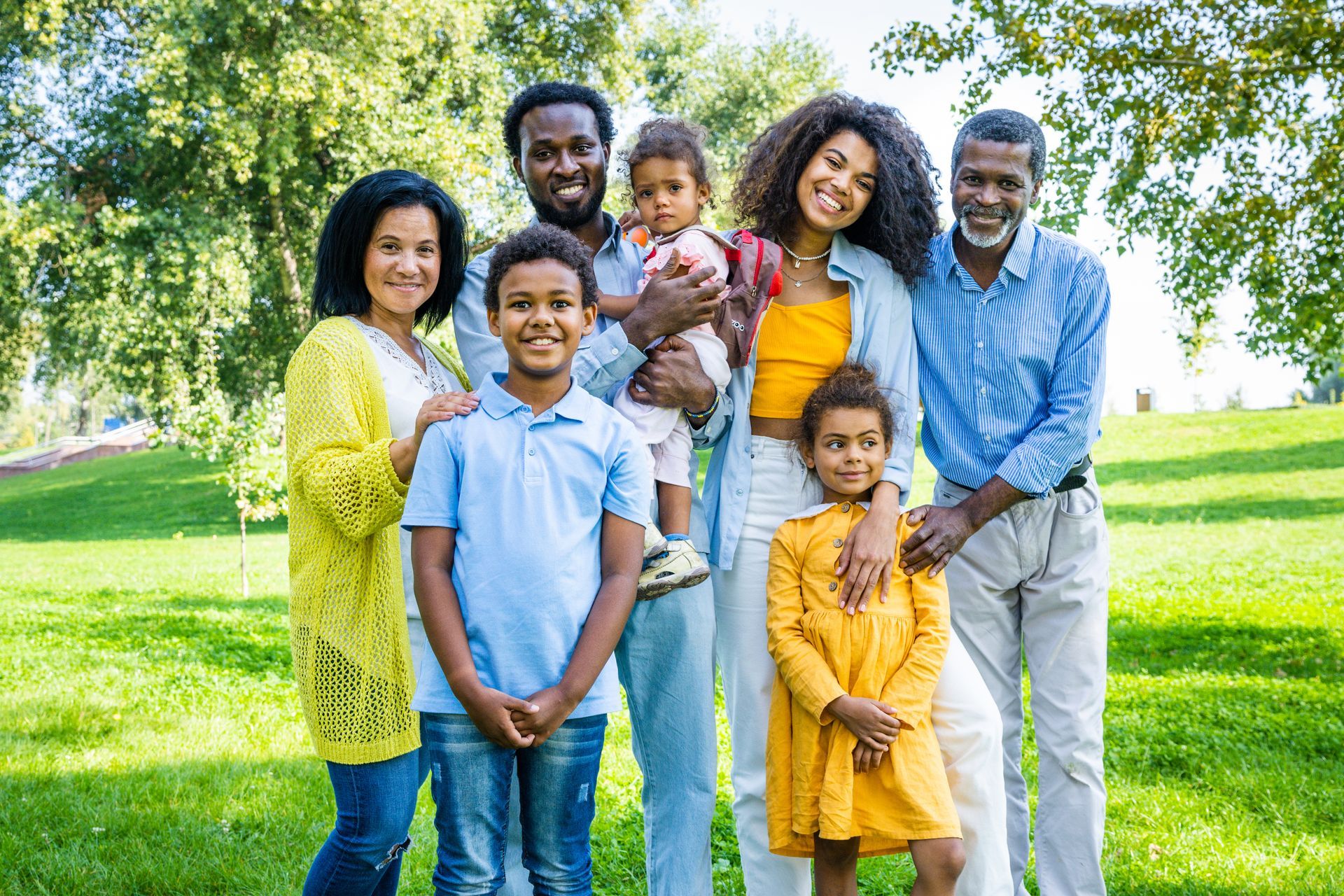 Happy Black family of seven posing in a park, smiling at camera.