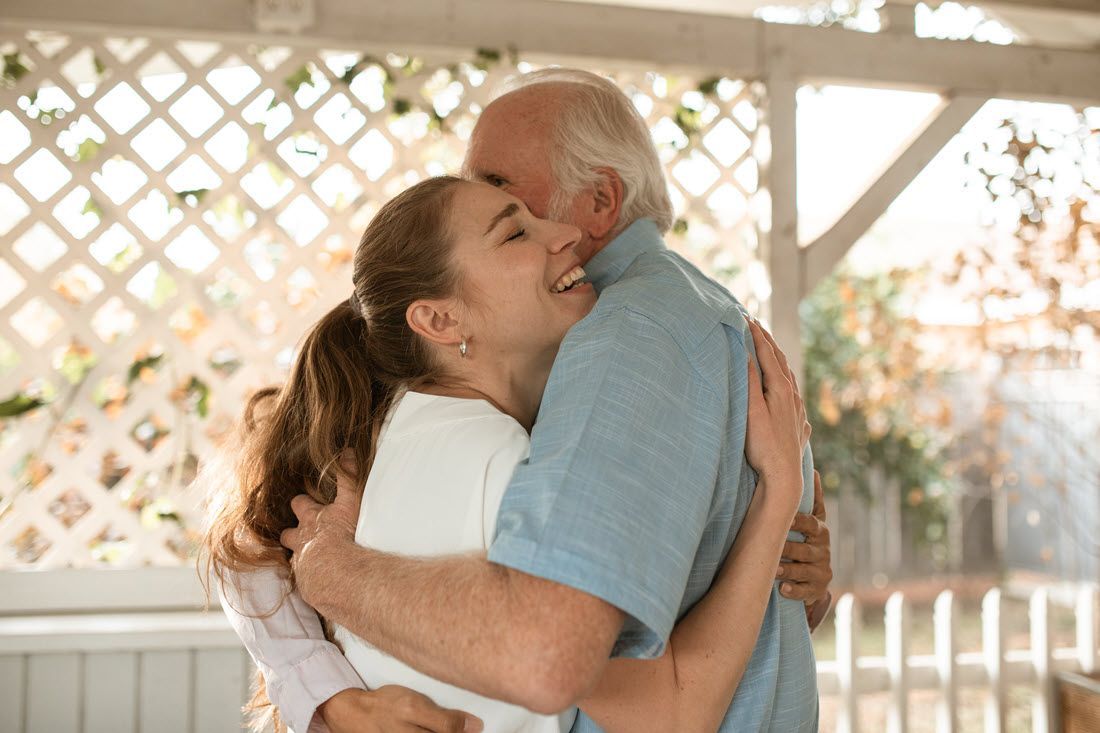 Two people hugging warmly in a sunlit outdoor gazebo with lattice walls