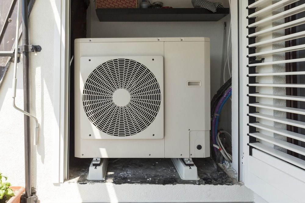 A White Heat Pump Is Sitting Inside of A Building Next to A Window — Sunworks Eco Plumbing In Torquay, VIC