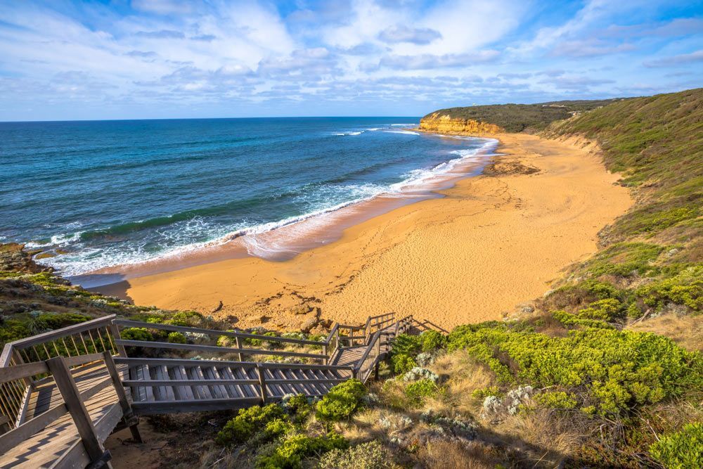 A Wooden Staircase Leading up To a Sandy Beach Next to The Ocean — Sunworks Eco Plumbing In Anglesea, VIC