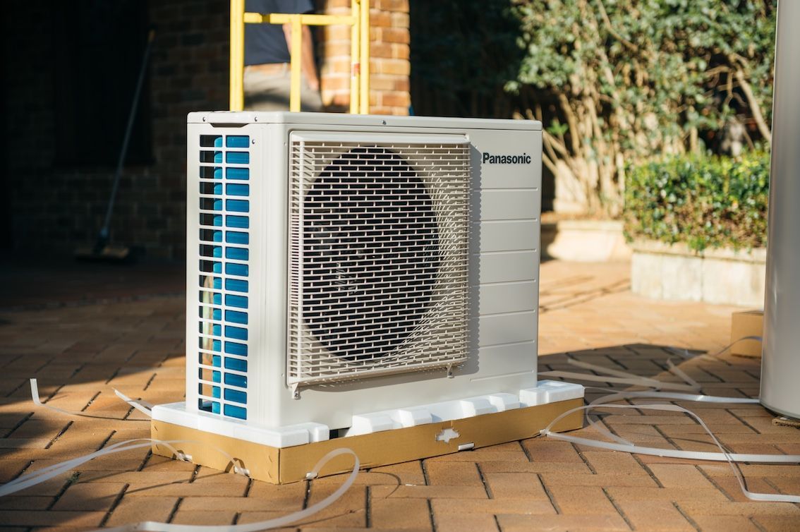 A Man Is Installing a Heat Pump on The Side of A Building — Sunworks Eco Plumbing In Altona, VIC
