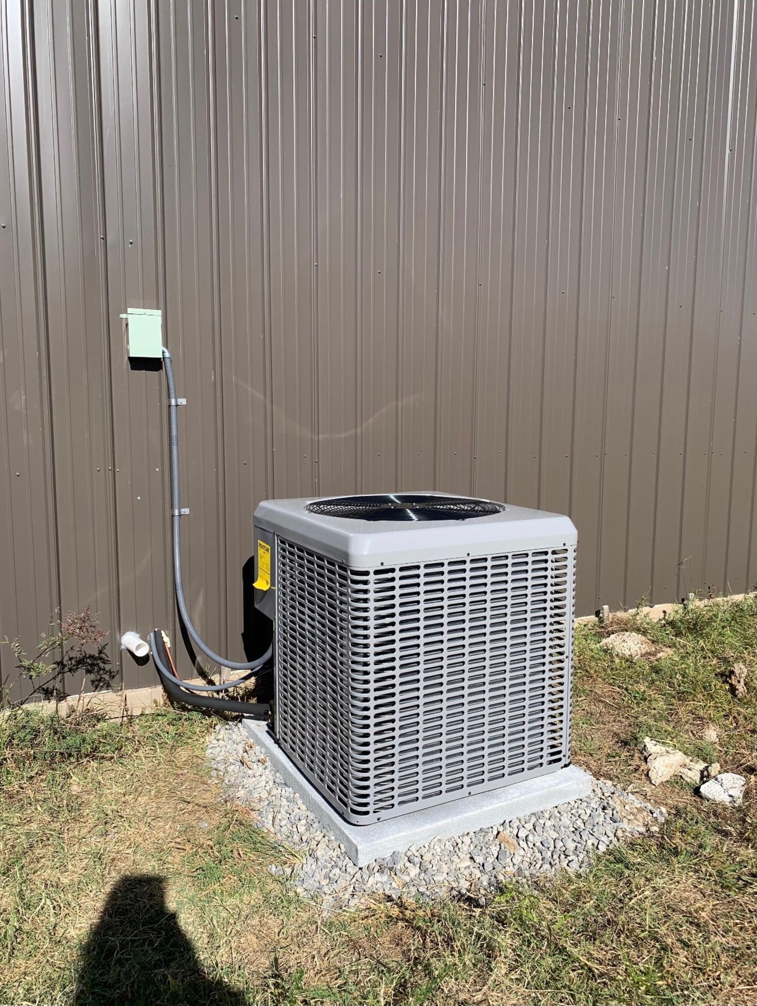 An air conditioner is sitting in the grass next to a fence.