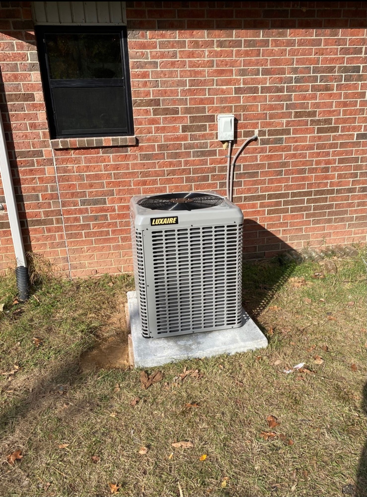 An air conditioner is sitting on the side of a brick house.
