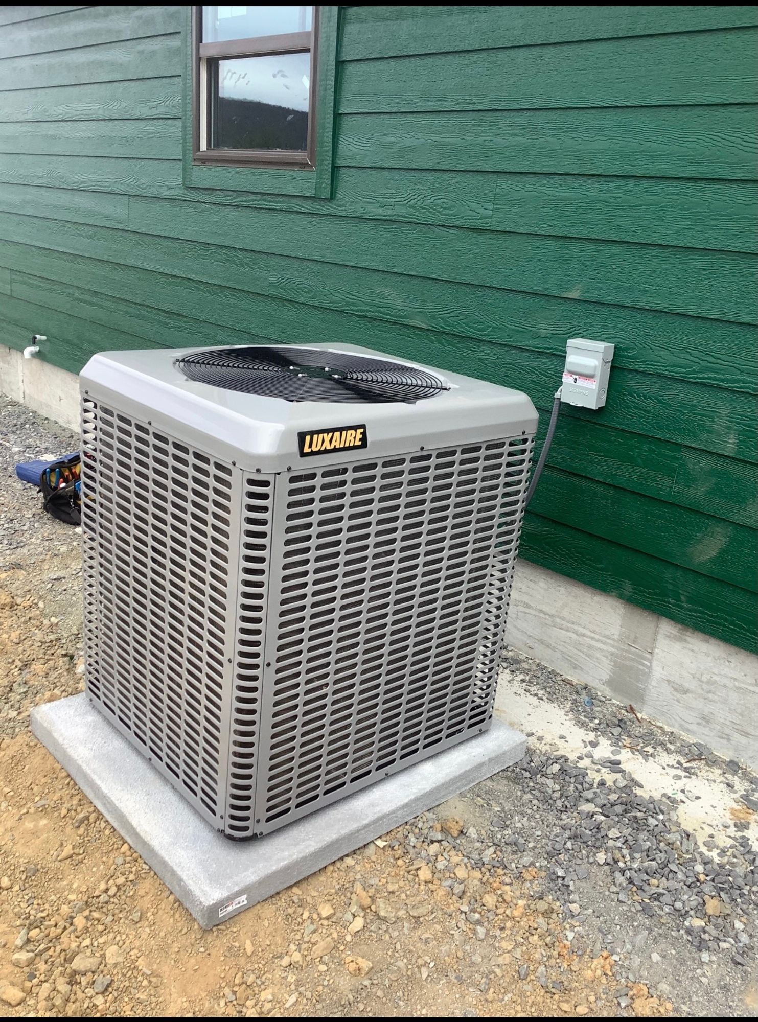 A large air conditioner is sitting outside of a green house.