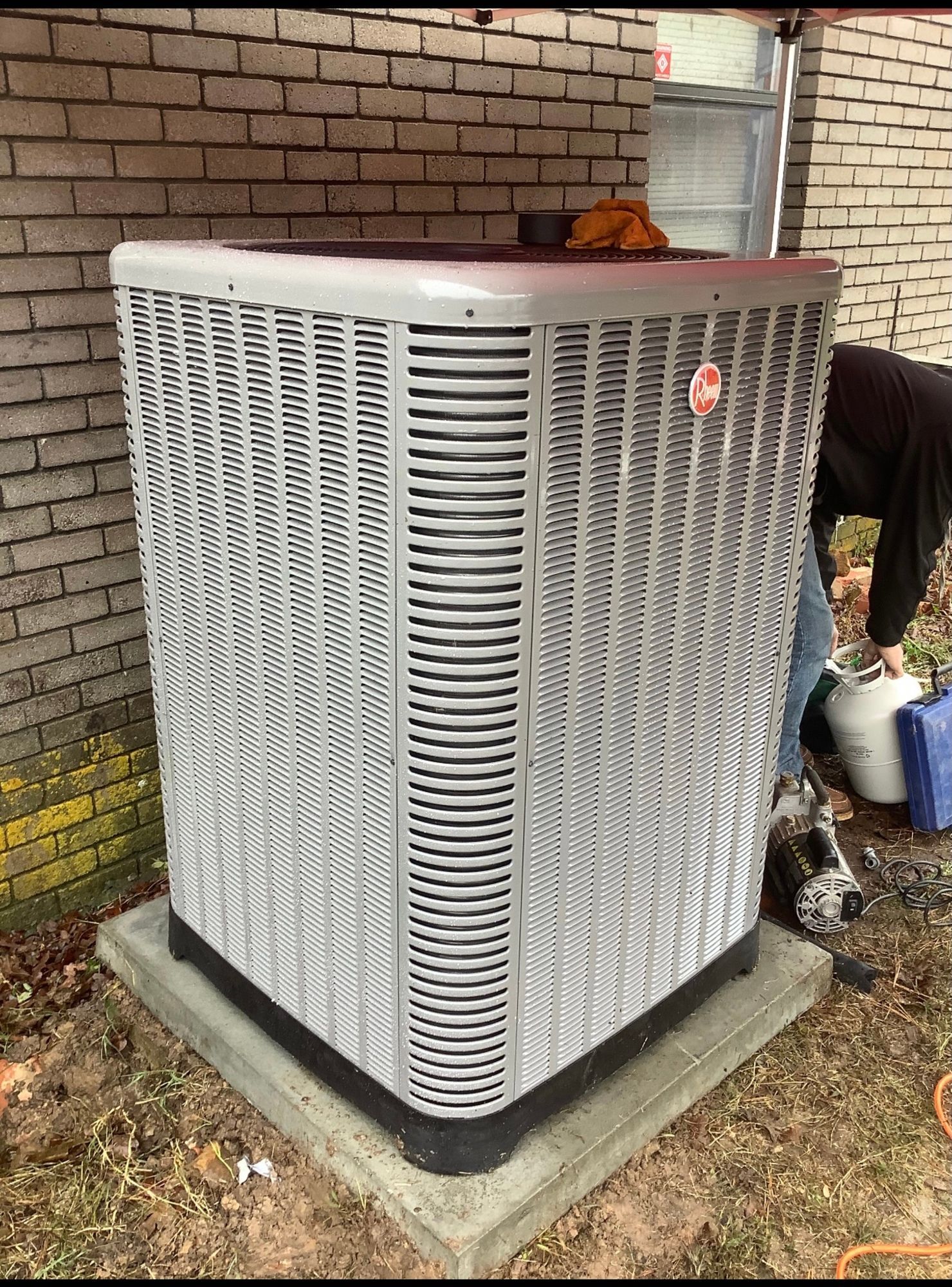 A man is working on an air conditioner outside of a brick building.