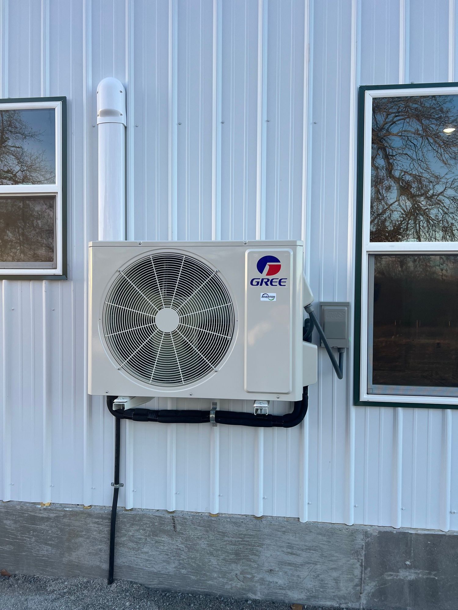 A white air conditioner is mounted on the side of a building next to two windows.