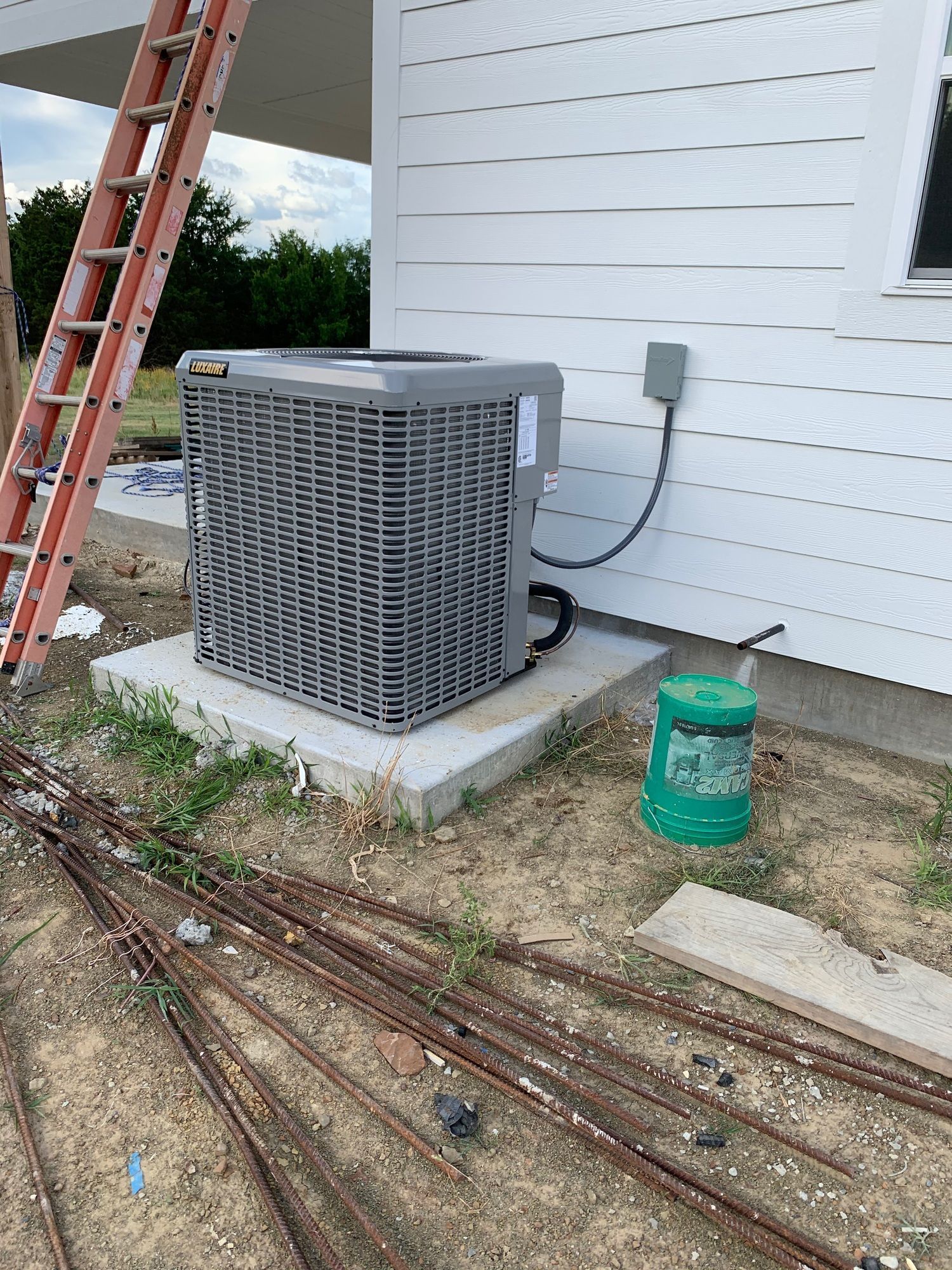 An air conditioner is sitting on the side of a house next to a ladder.