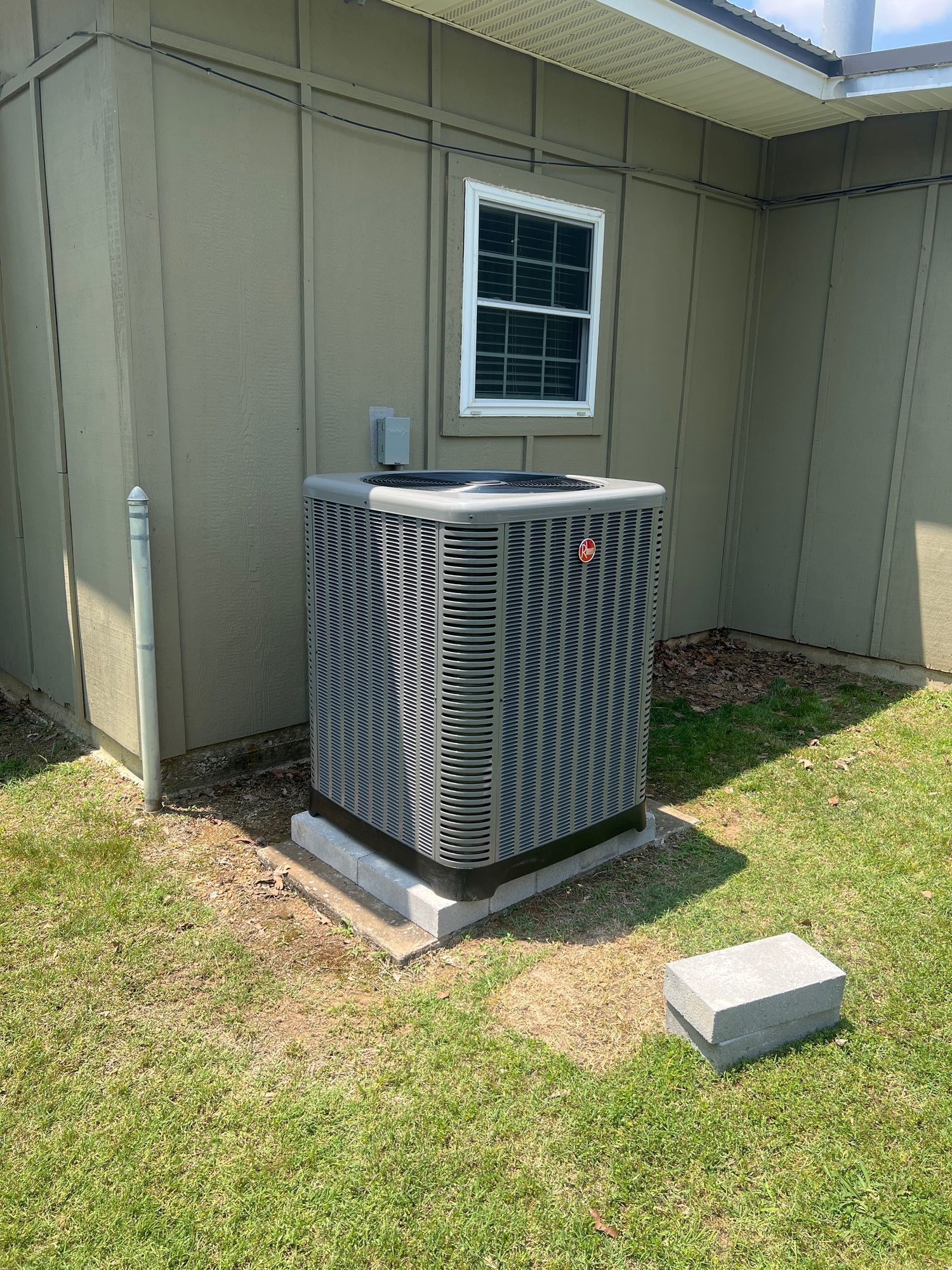 An air conditioner is sitting on the side of a house next to a window.