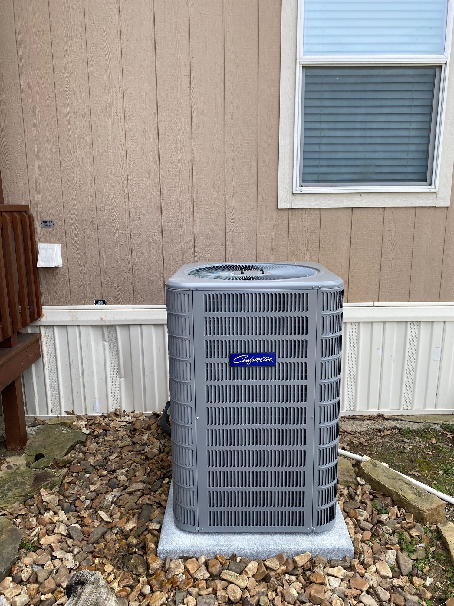 A gray air conditioner is sitting in front of a house.