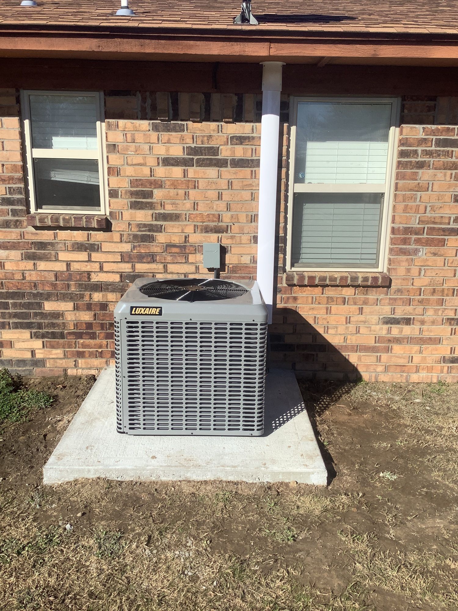 An air conditioner is sitting on the side of a brick house.