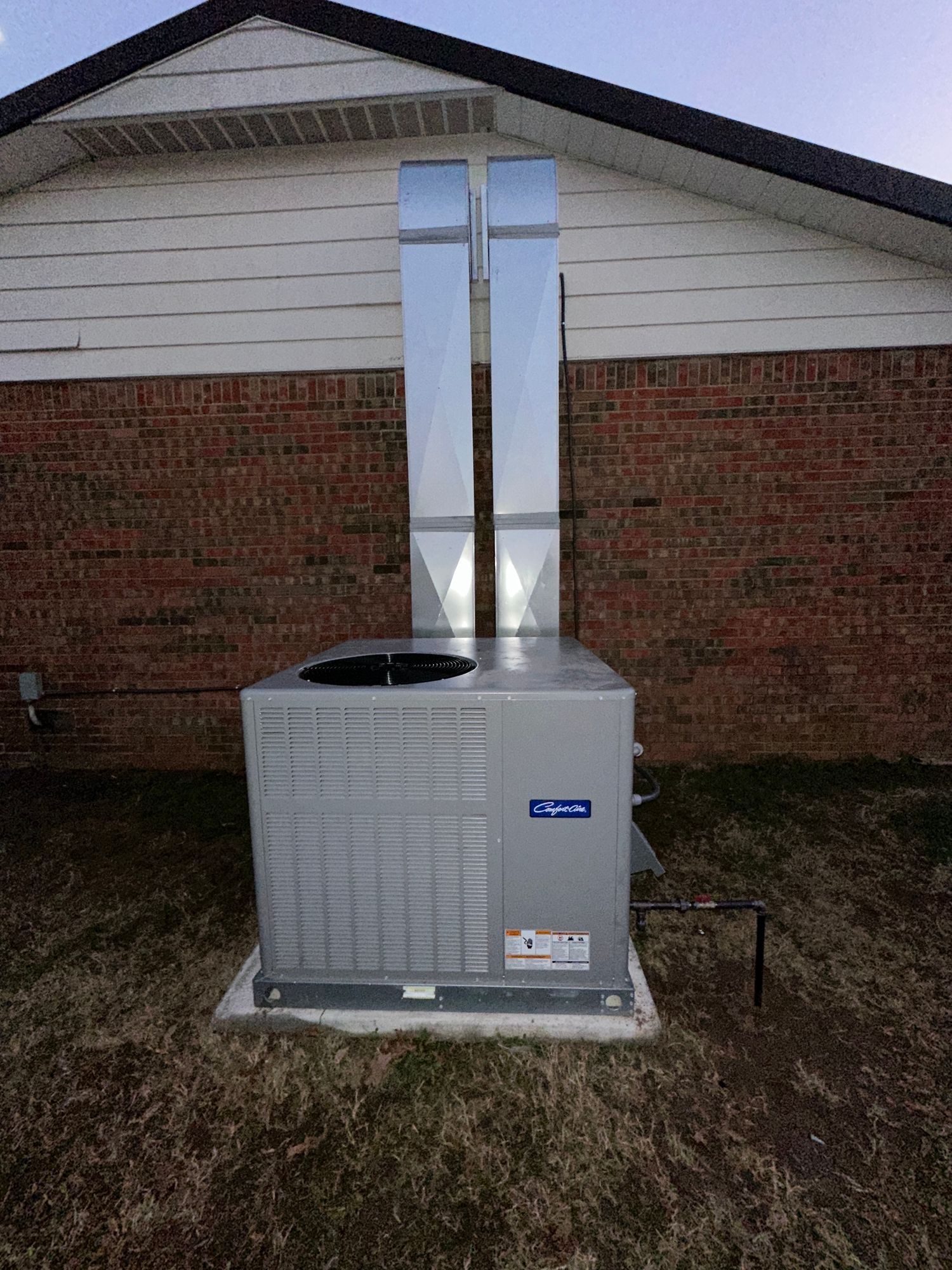 A large air conditioner is sitting outside of a brick house.