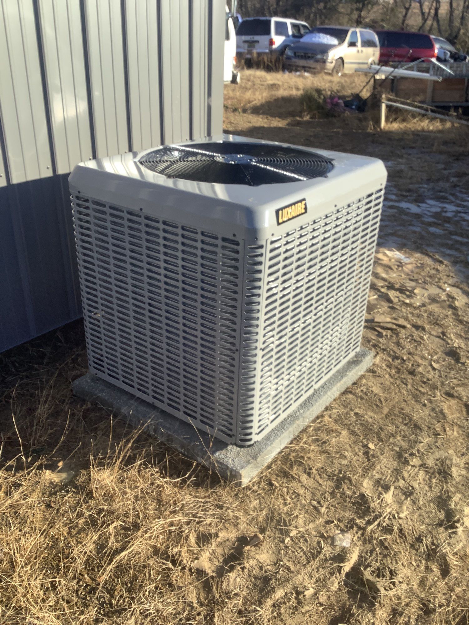 A large air conditioner is sitting in the dirt next to a building.