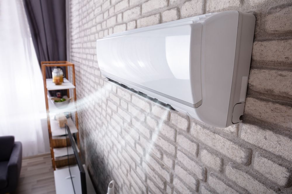 A white air conditioner is hanging on a brick wall in a living room.