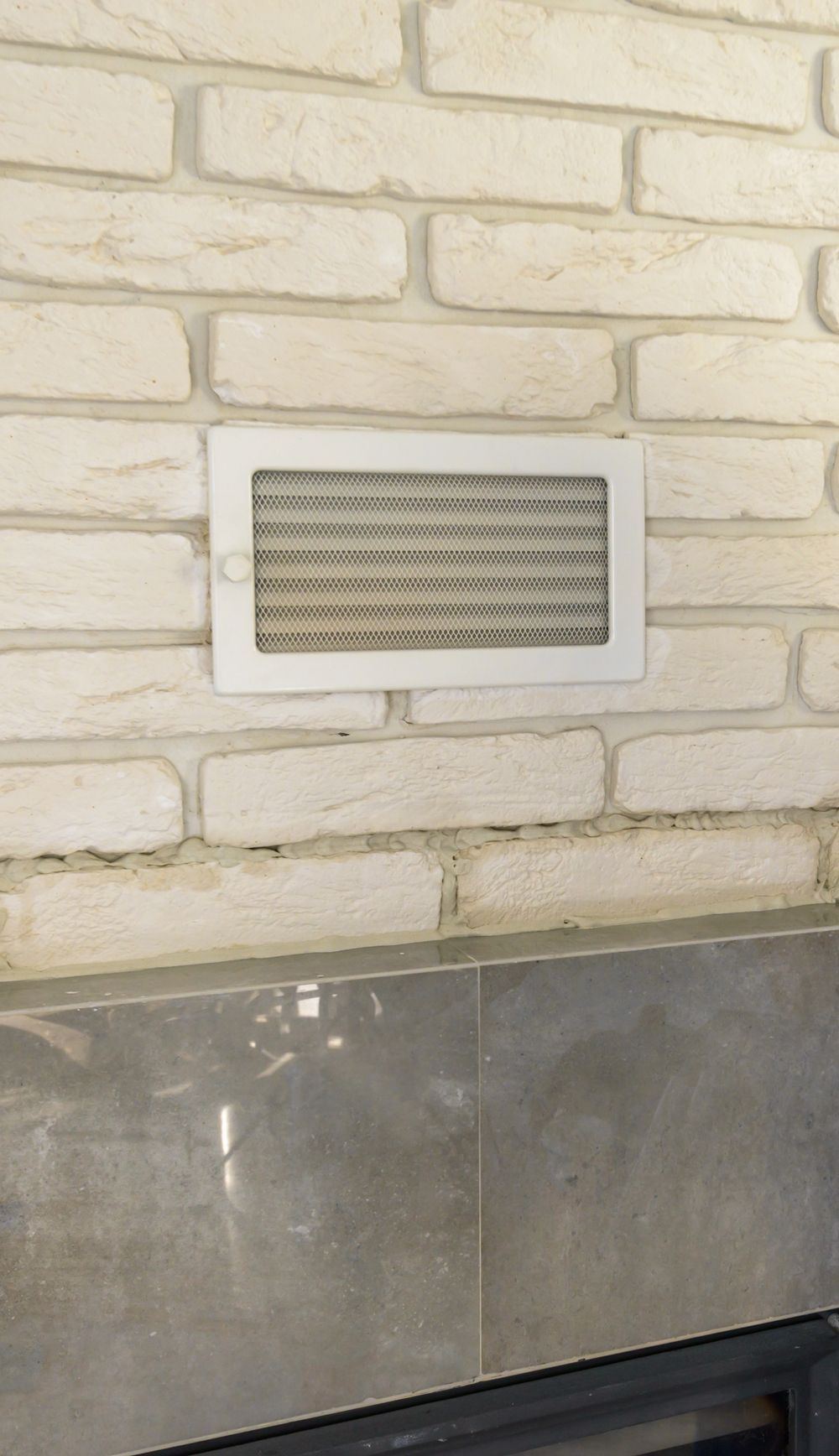 A white brick wall with a white vent on it