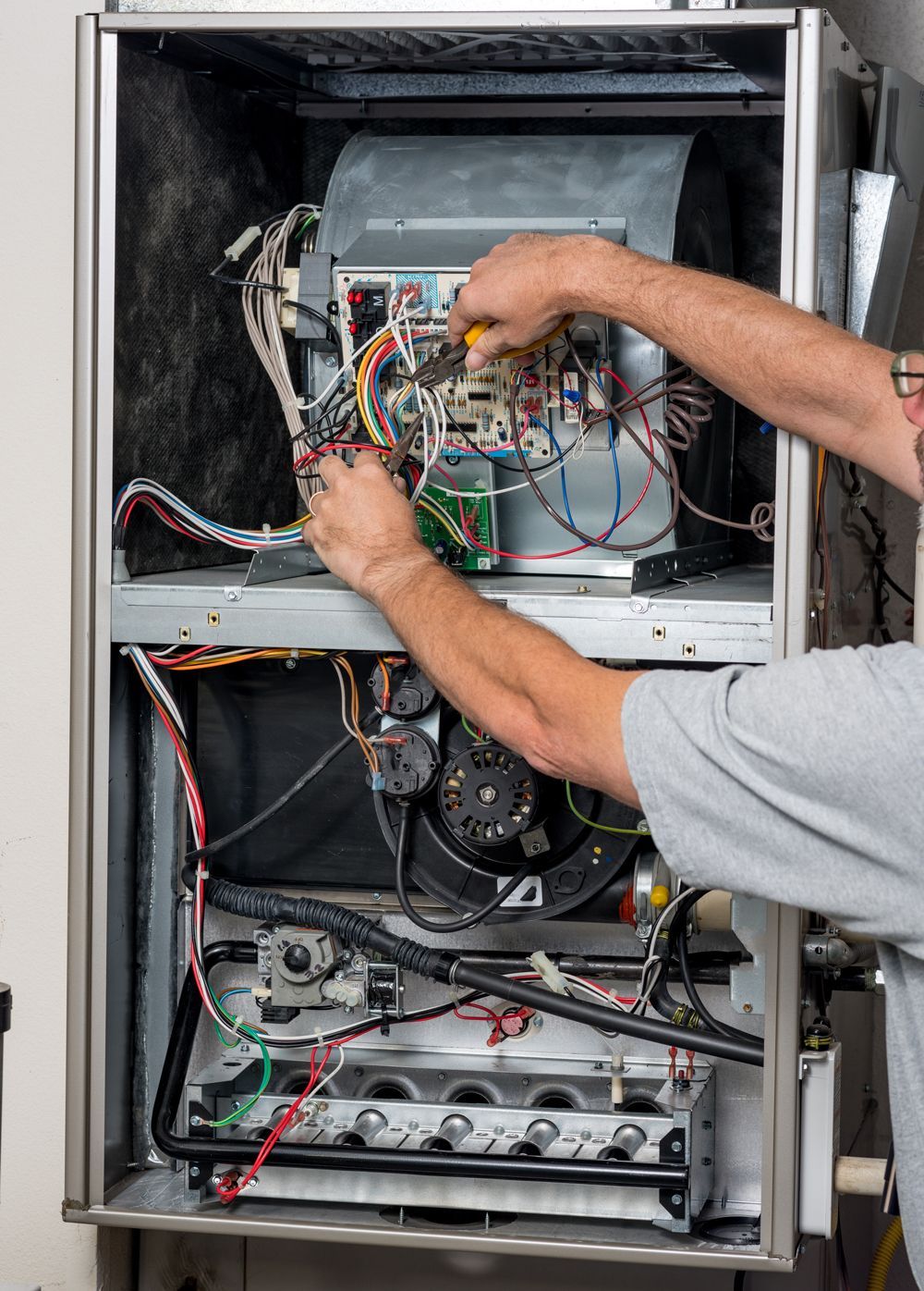 A man is working on an air conditioner with a pair of pliers.