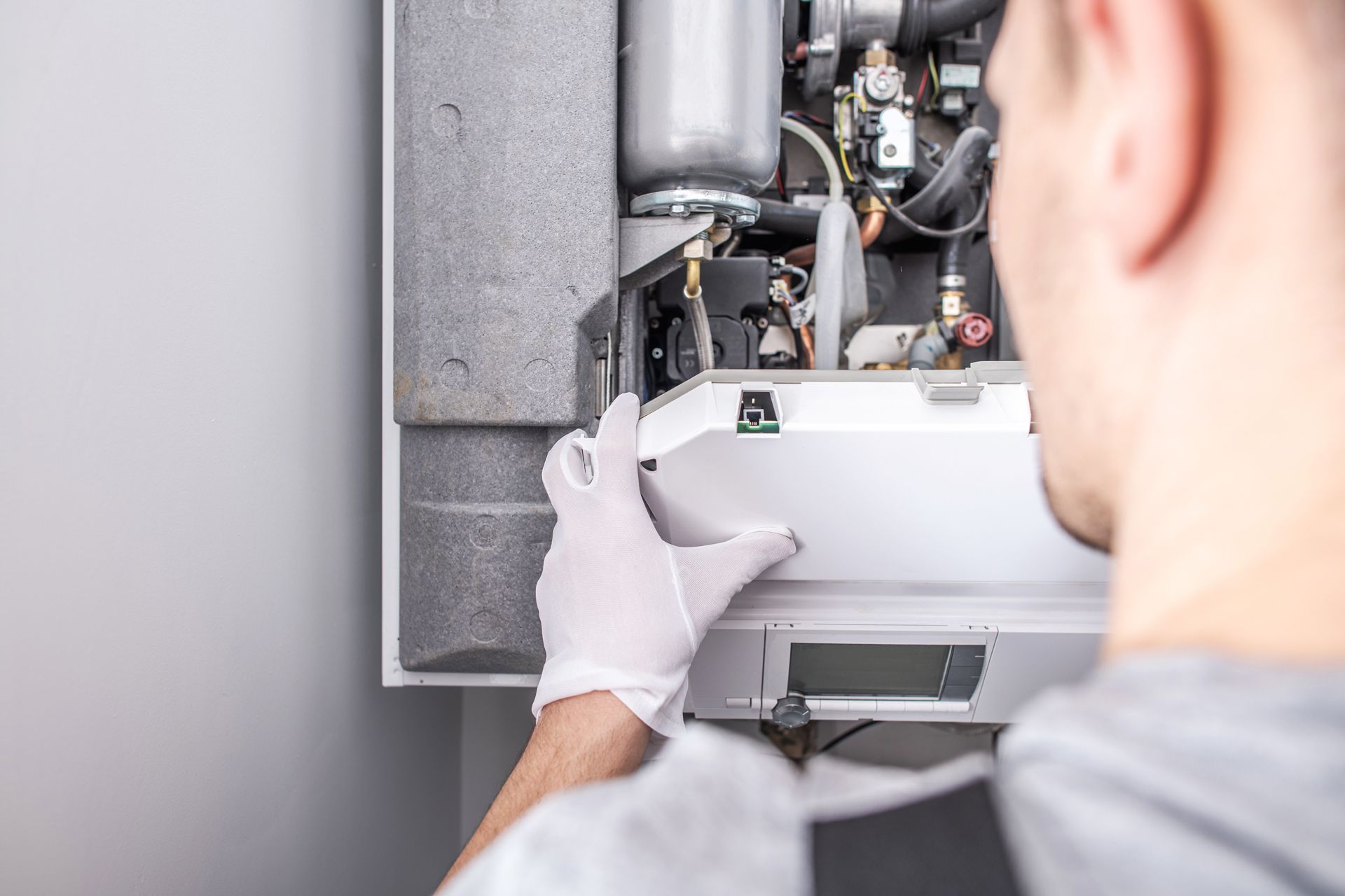 A man wearing white gloves is working on a boiler.