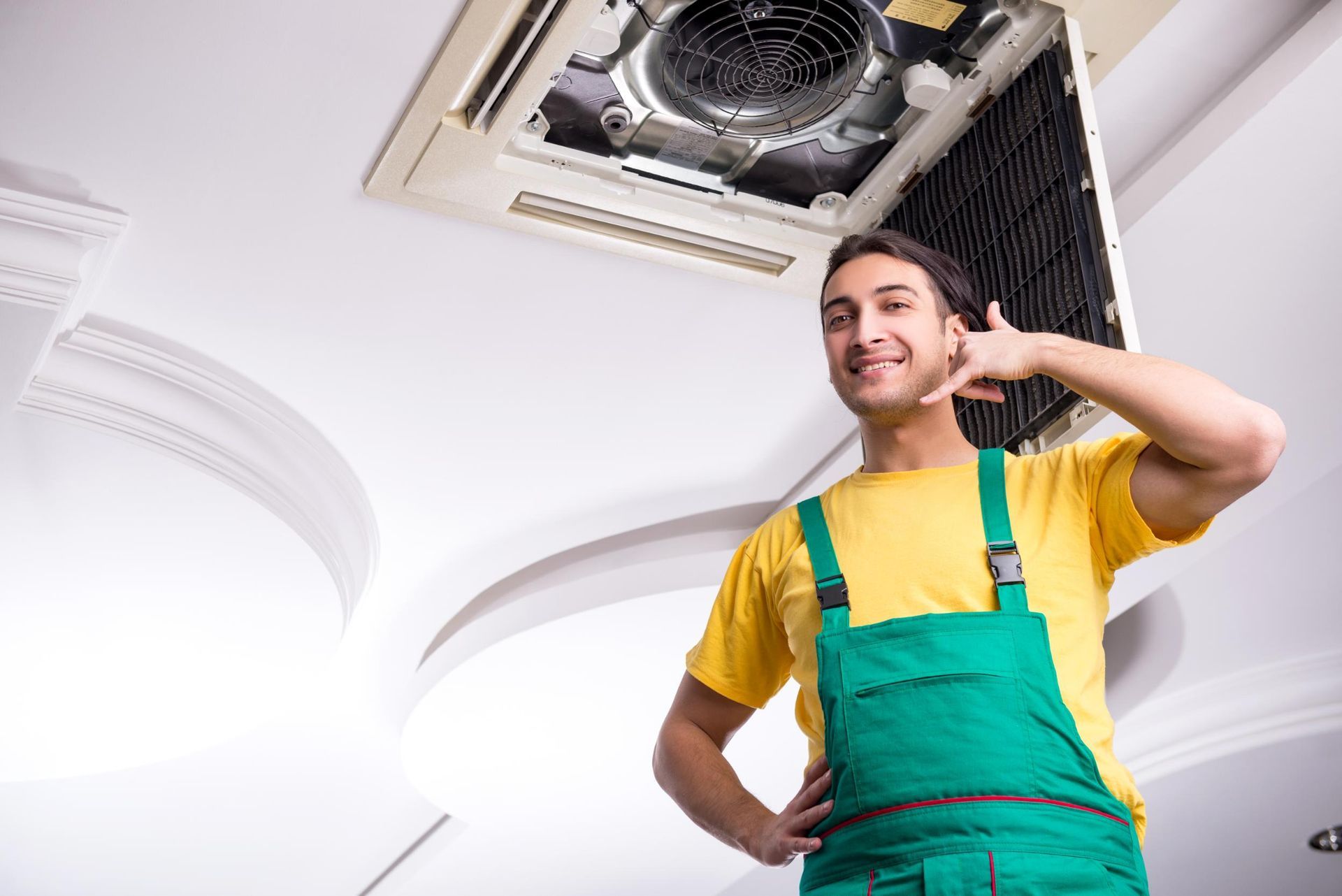 A man in green overalls is standing under a ceiling fan.