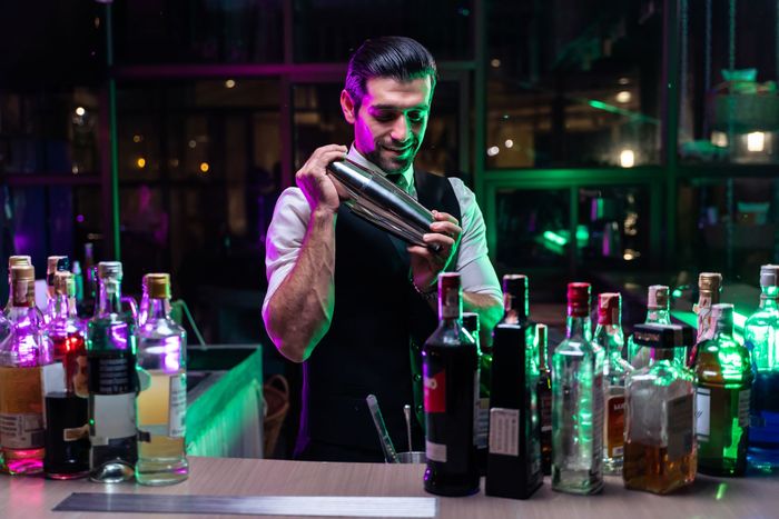A bartender is shaking a drink in a shaker at a bar.