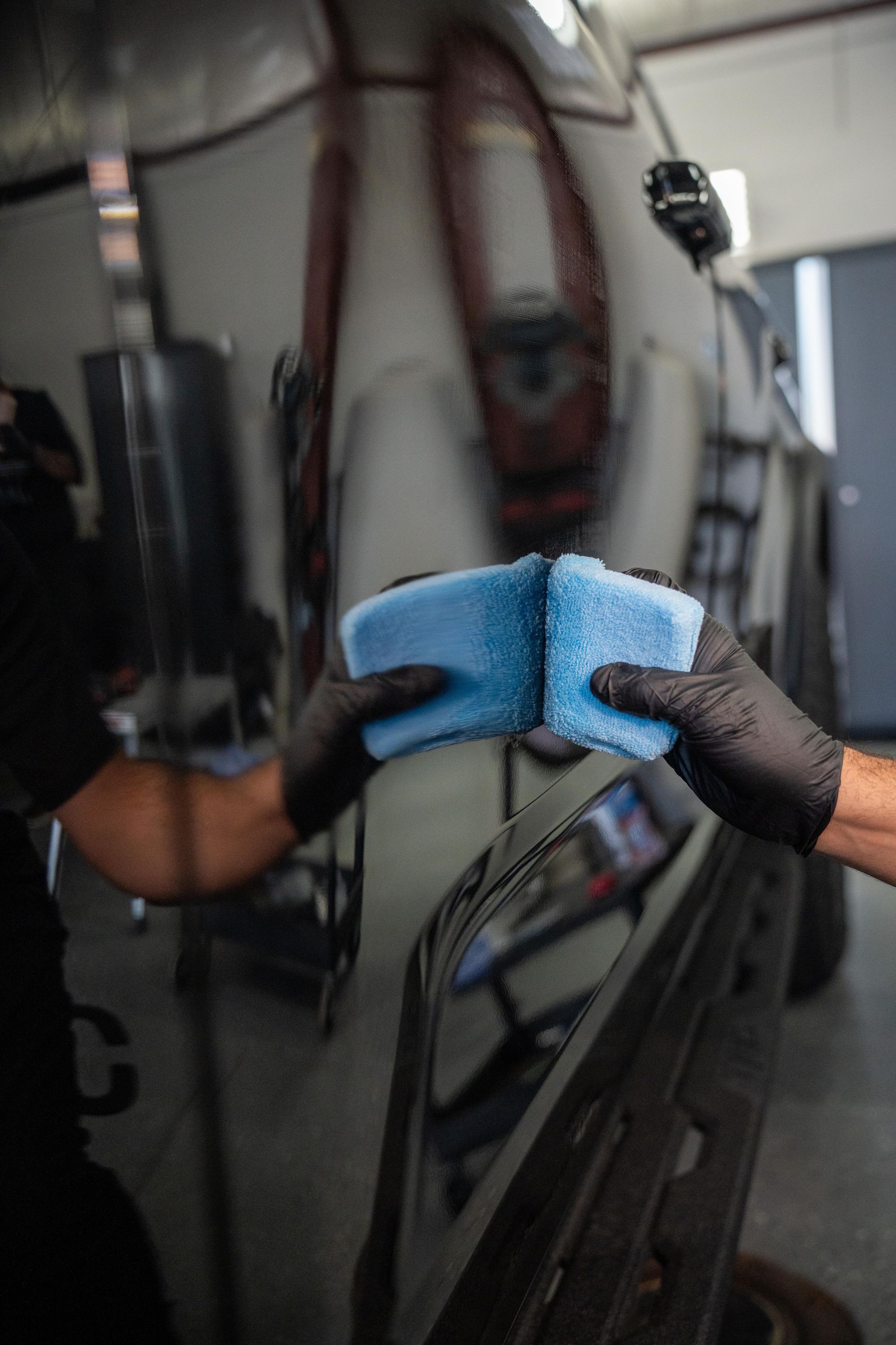 Person in black gloves detailing black car paint with a blue sponge.