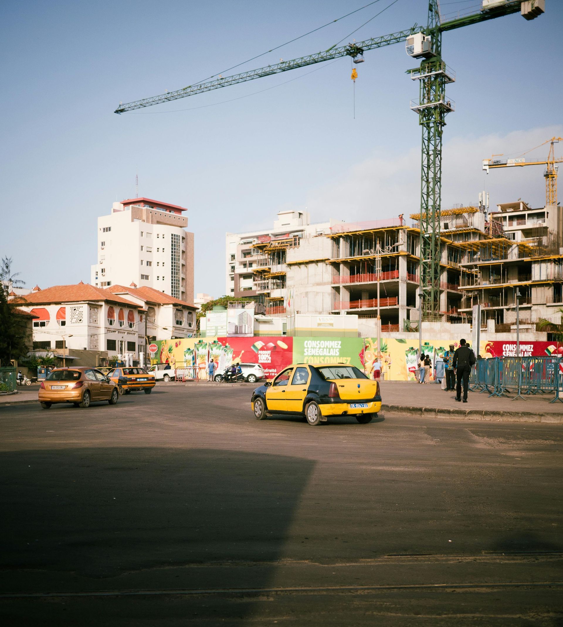 Busy city street with a yellow taxi, construction crane, and apartment buildings under a clear sky