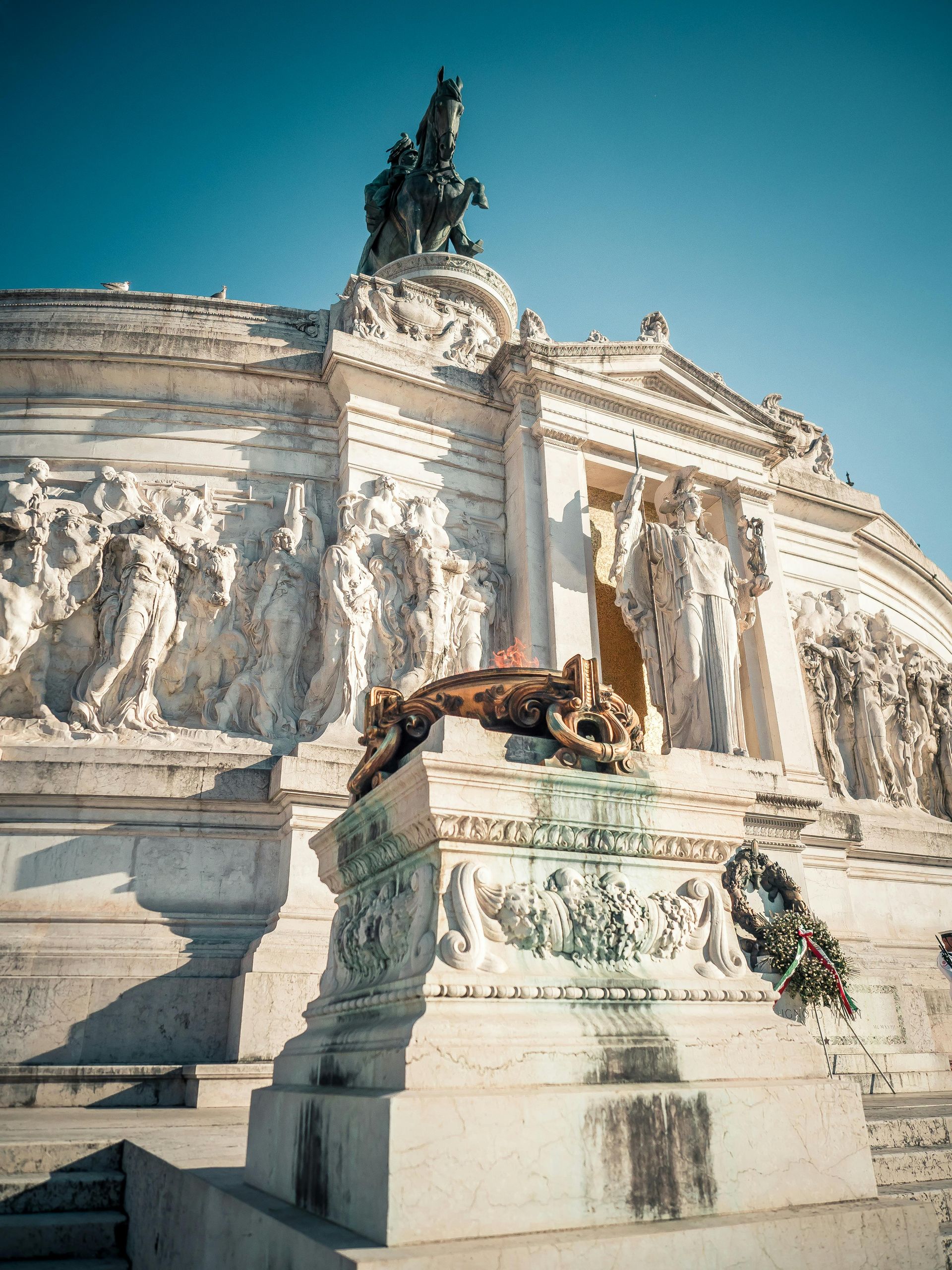 White marble monument with sculpted figures and an equestrian statue against a blue sky