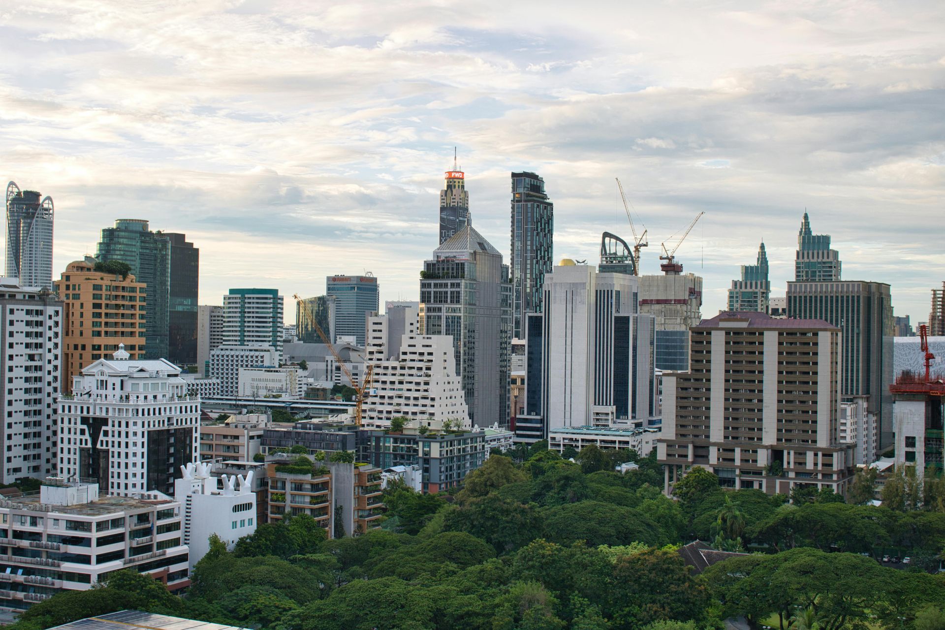 City skyline with high-rise buildings above a green treeline under a cloudy sky