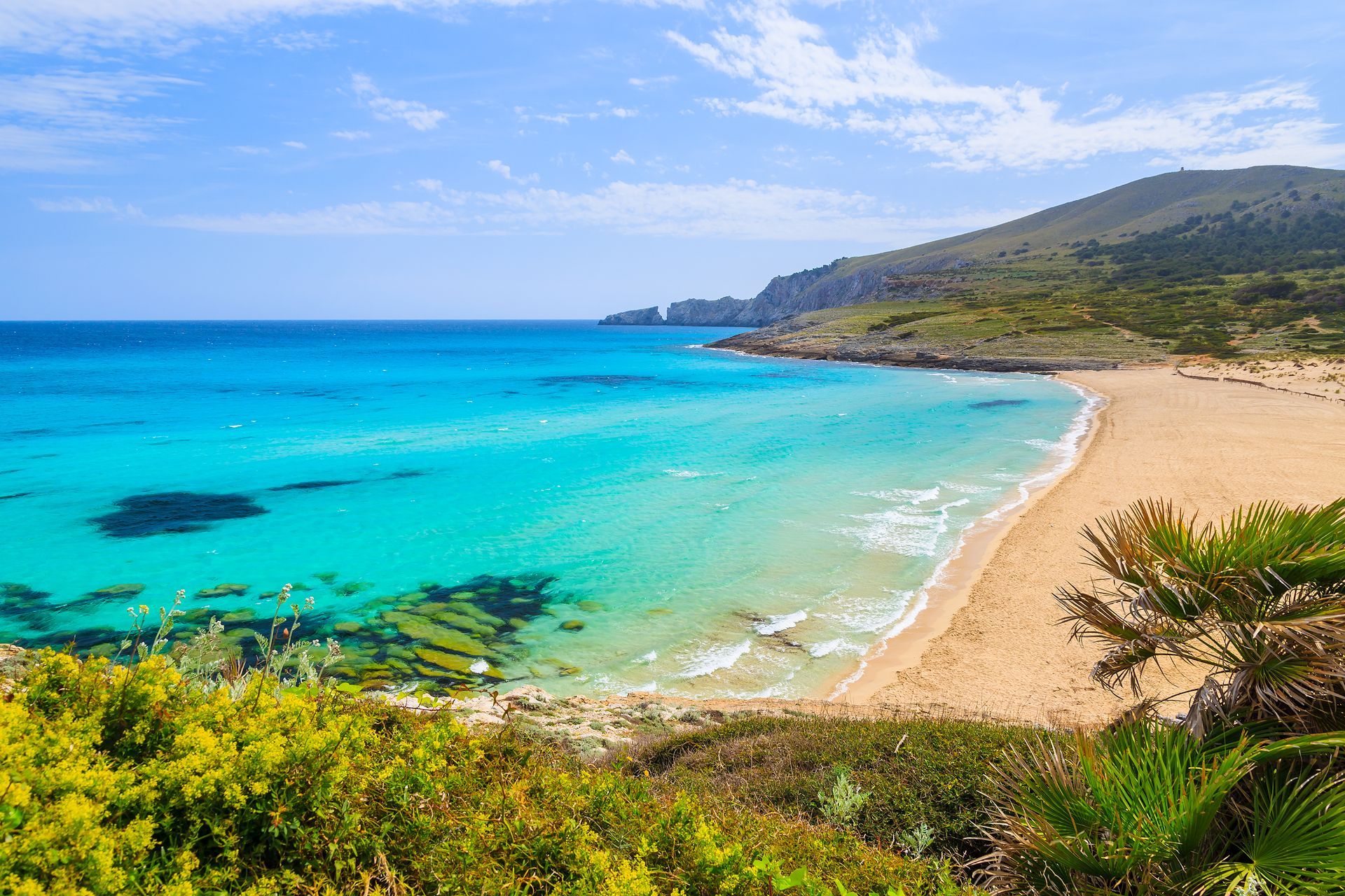 Turquoise ocean beside a sandy beach with green hills under a blue sky