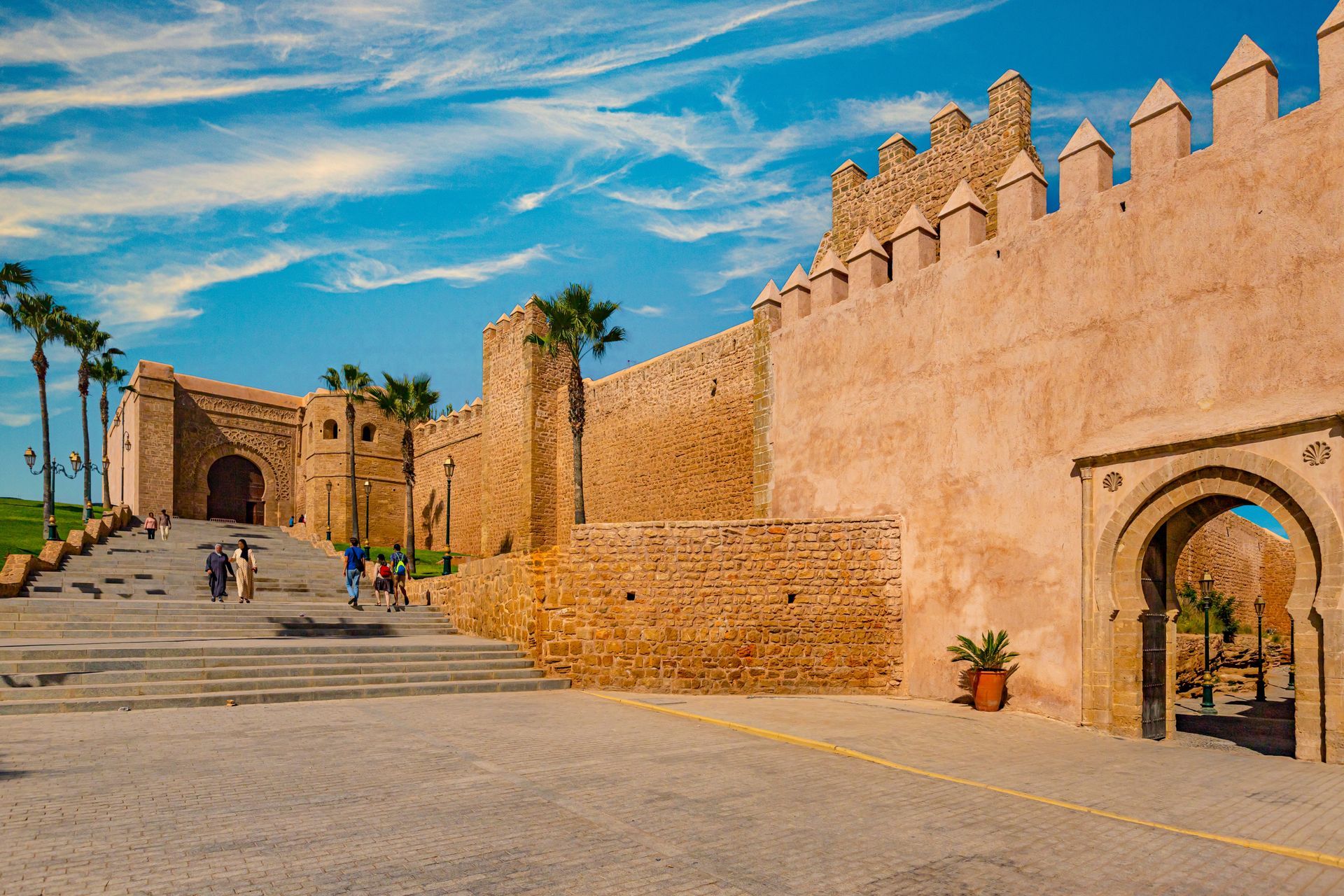 Sunlit stone fortress wall and arched gate beside a wide path under a blue sky