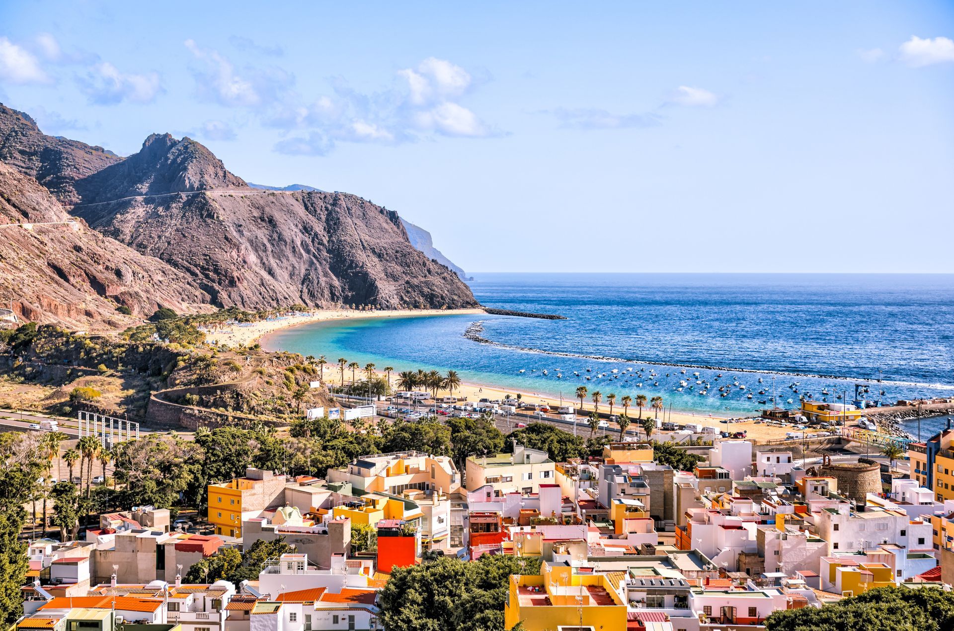 Coastal town with white buildings, rocky mountains, turquoise bay, and blue sea under a clear sky