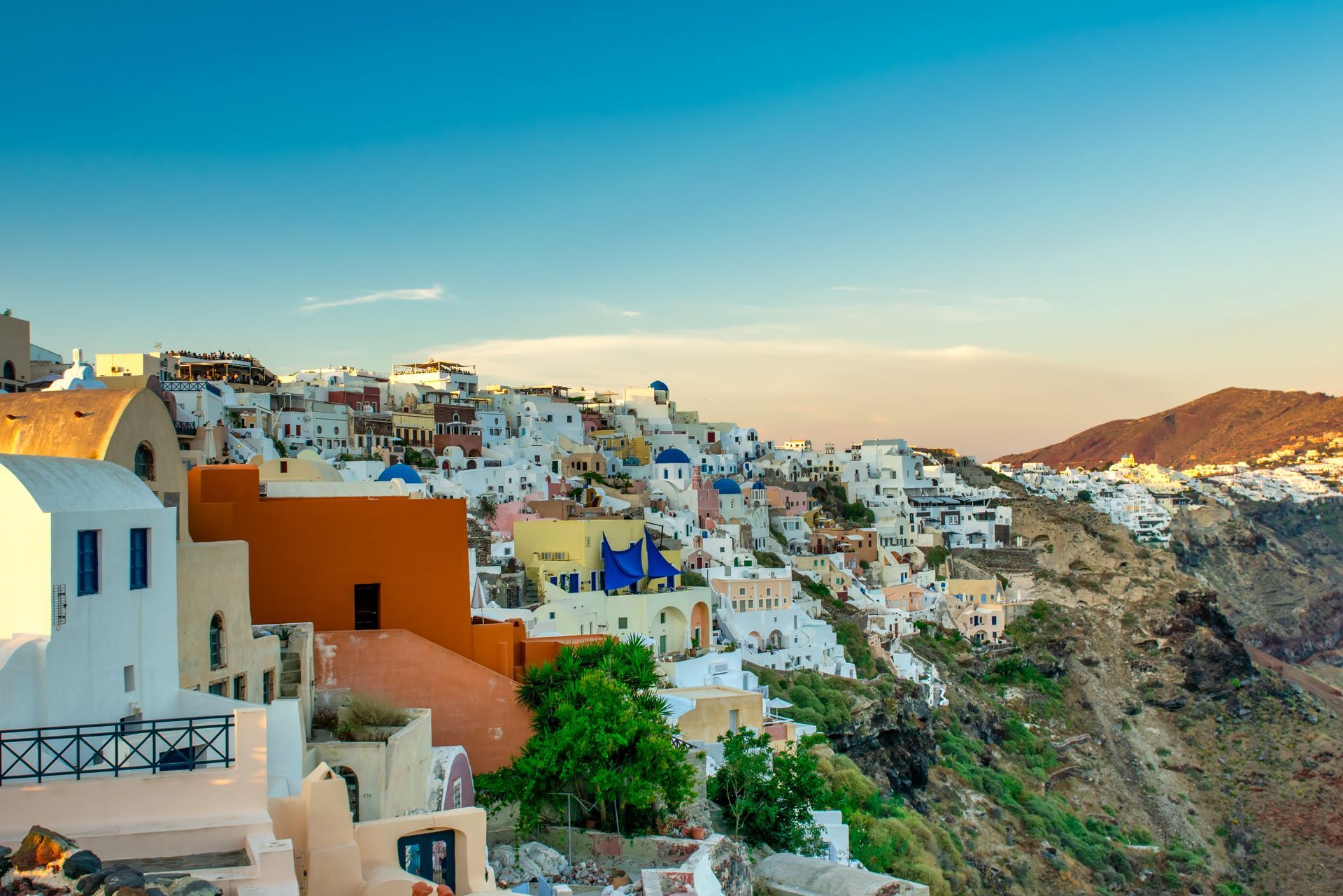 Colorful cliffside buildings overlooking a blue sea at sunset, likely in a Mediterranean coastal village