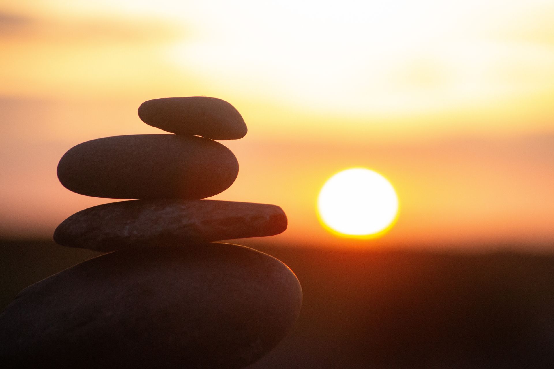 Stacked stones silhouetted against a glowing sunset over calm water