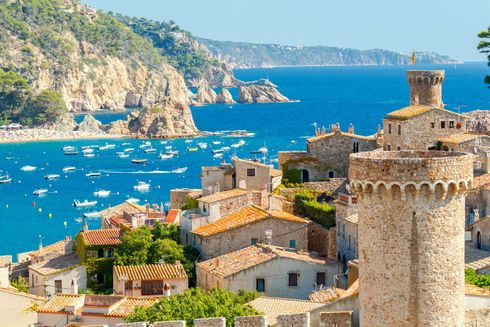 Stone coastal village overlooking a bright blue bay with boats and rocky cliffs