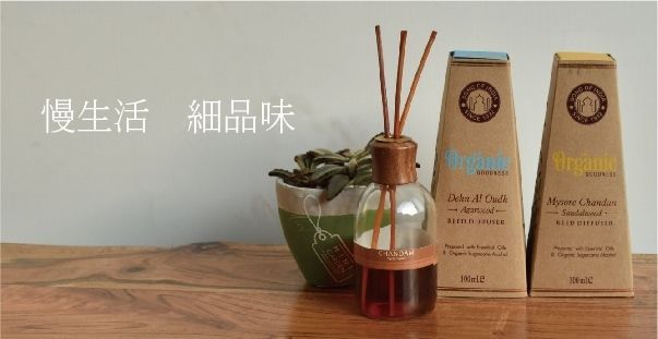 Reed diffuser and scent bottles on a wooden surface, next to a potted plant against a neutral background.