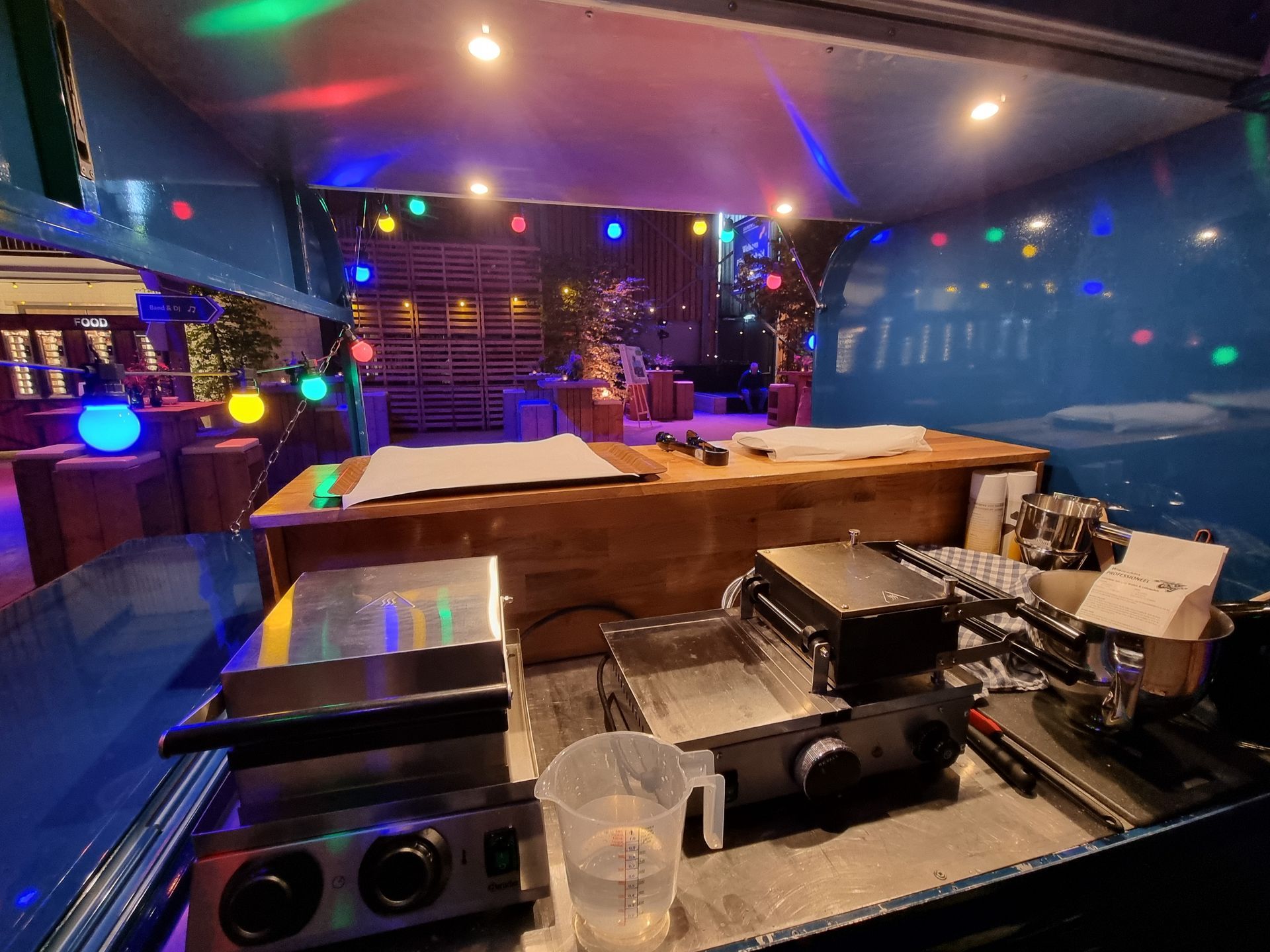Het interieur van de foodtruck is verlicht met gekleurde lampen en bevat kookapparatuur en een houten toonbank.
