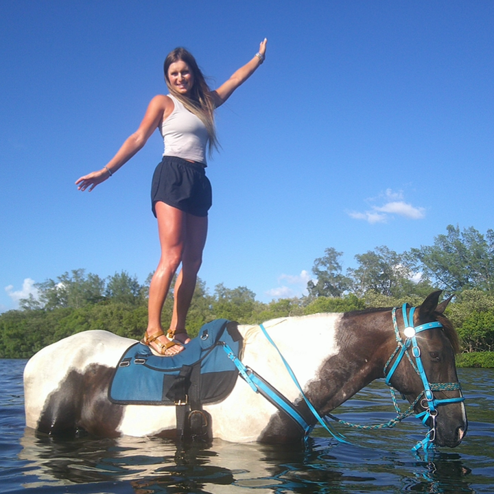 girl horse back riding touching other horse