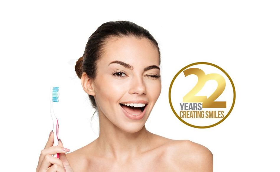 Smiling woman holding a toothbrush beside a gold “22 years creating smiles” logo.