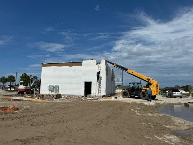 A yellow crane is lifting a white building in a dirt field.