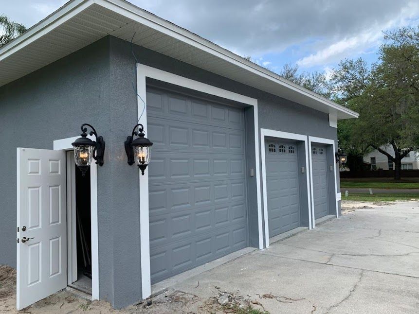 A gray garage with three garage doors and a white trim.