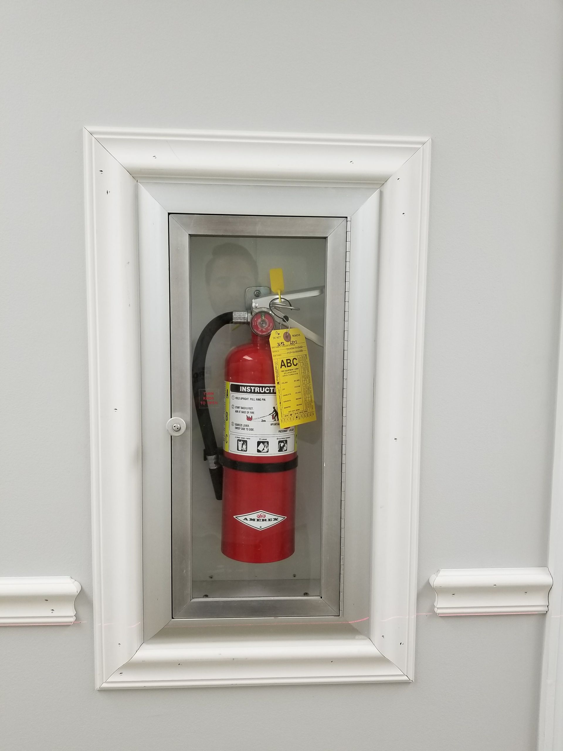 A red fire extinguisher is in a white frame on a wall.