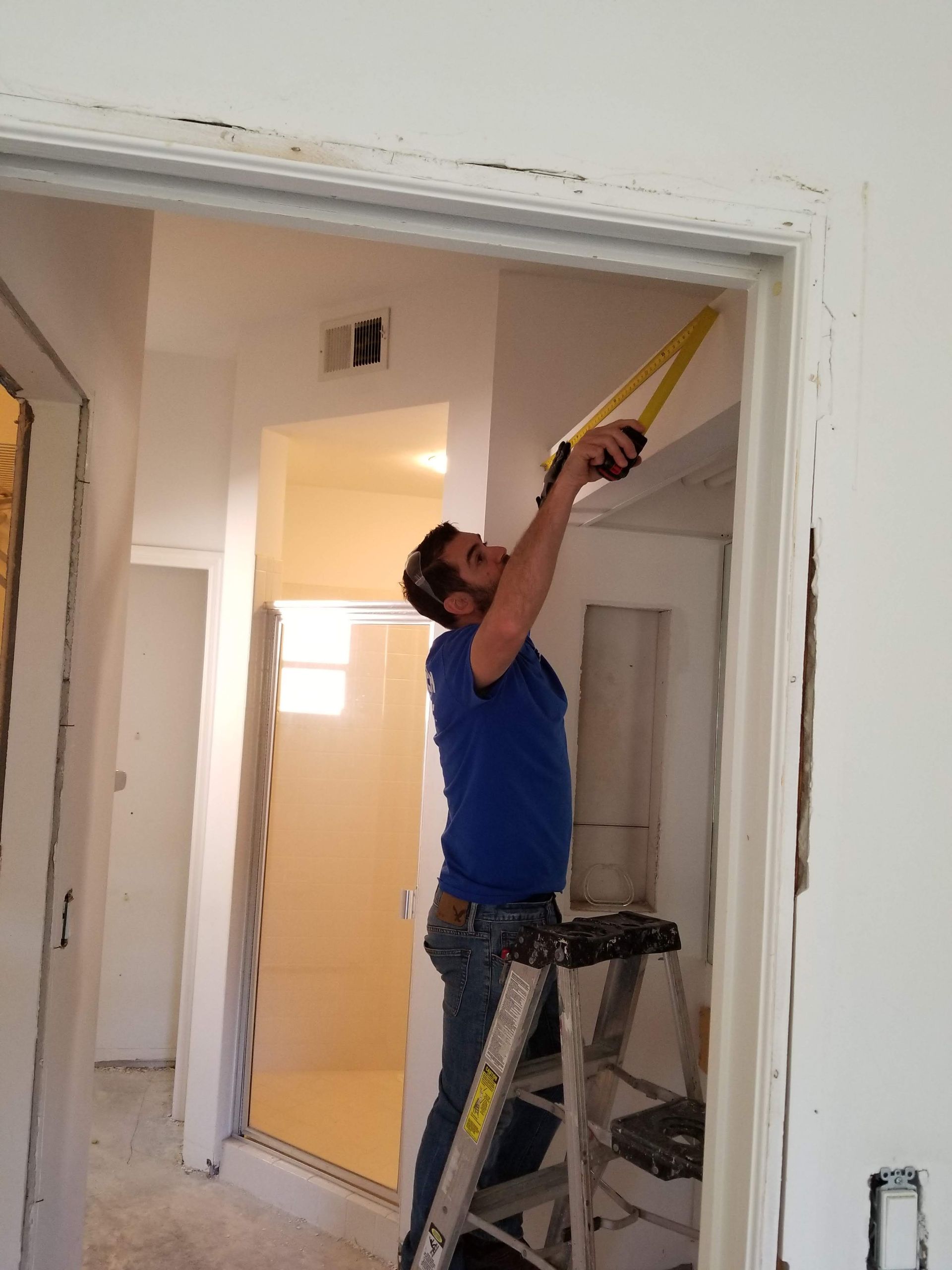 A man on a ladder measuring a door with a tape measure